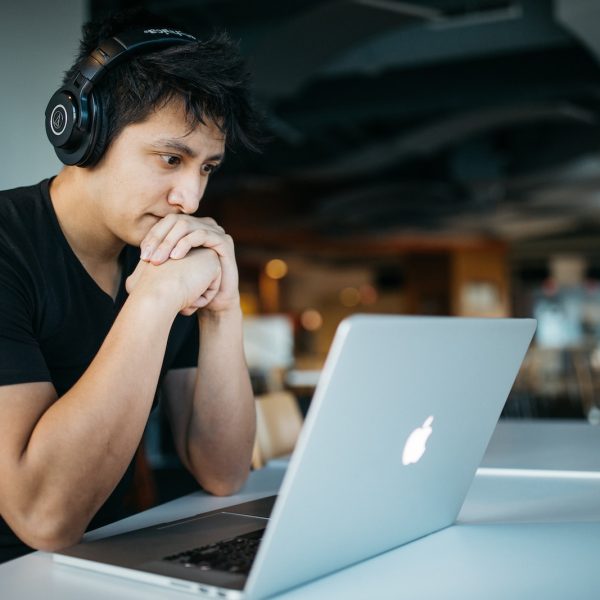 man wearing headphones while sitting on chair in front of MacBook