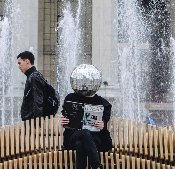 person sitting on wooden accordion bench while reading magazine at the back of water fountain